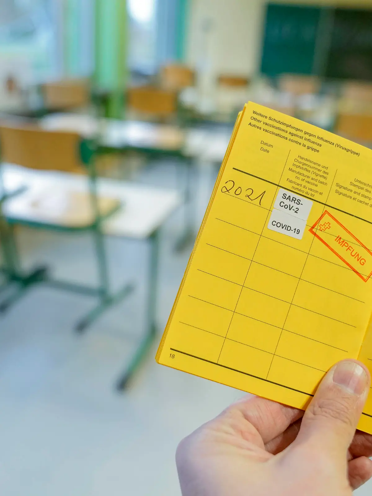  Symbolbild Schule und Klassenzimmer im Lockdown Symbolfoto eines Impfpass mit Impfstempel gegen das Coronavirus mit Klassenzimmer einer Schule im Hintergrund. Wann werden Lehrer und Schueler geimpft. Deutschland *** Symbolic image school and classroom in lockdown Symbolic photo of a vaccination certificate with vaccination stamp against the coronavirus with classroom of a school in the background When will teachers and students be vaccinated Germany