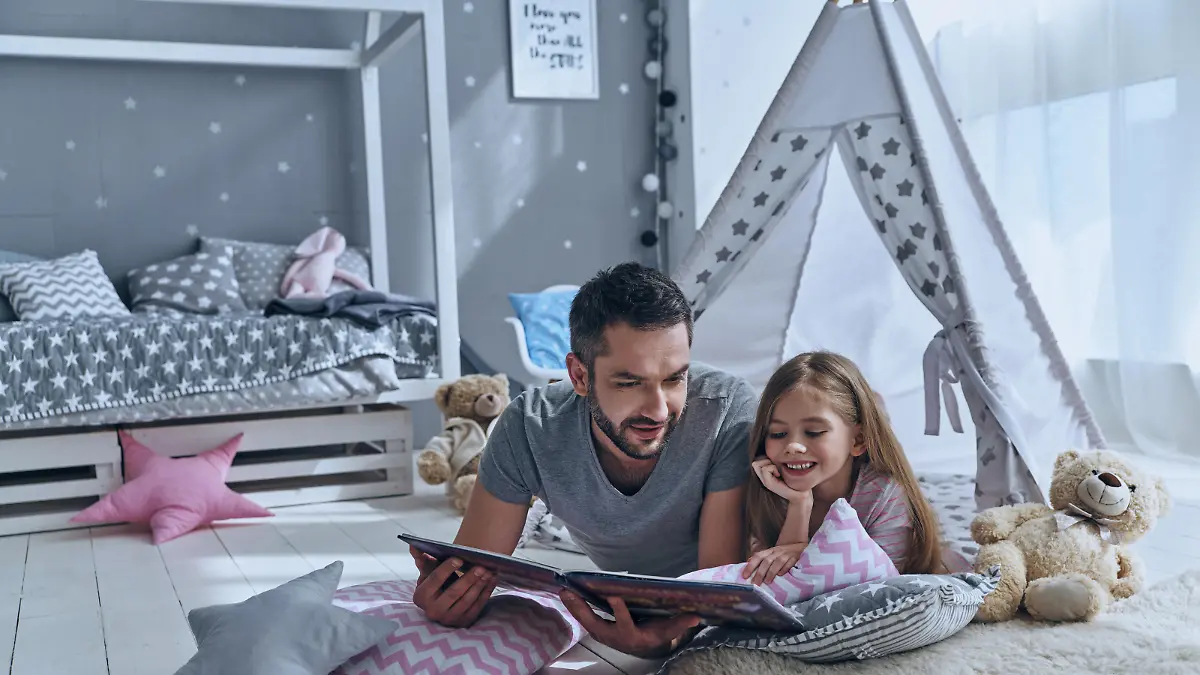 Father reading a book to his daughter while lying on the floor in bedroom