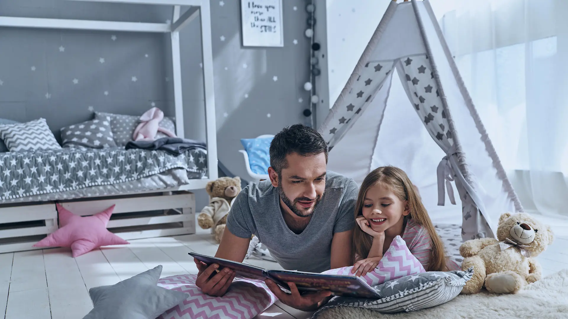 Father reading a book to his daughter while lying on the floor in bedroom