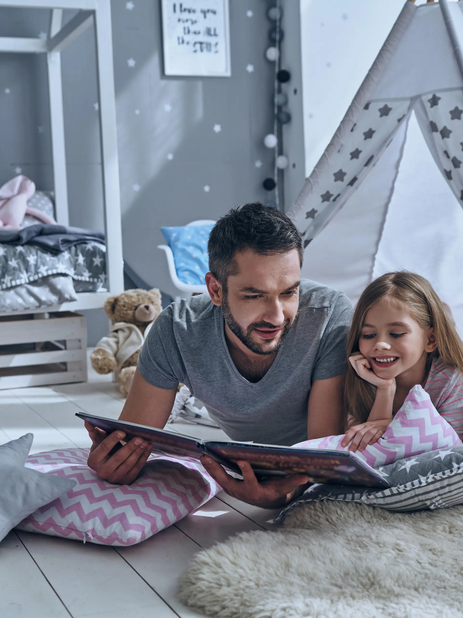 Father reading a book to his daughter while lying on the floor in bedroom