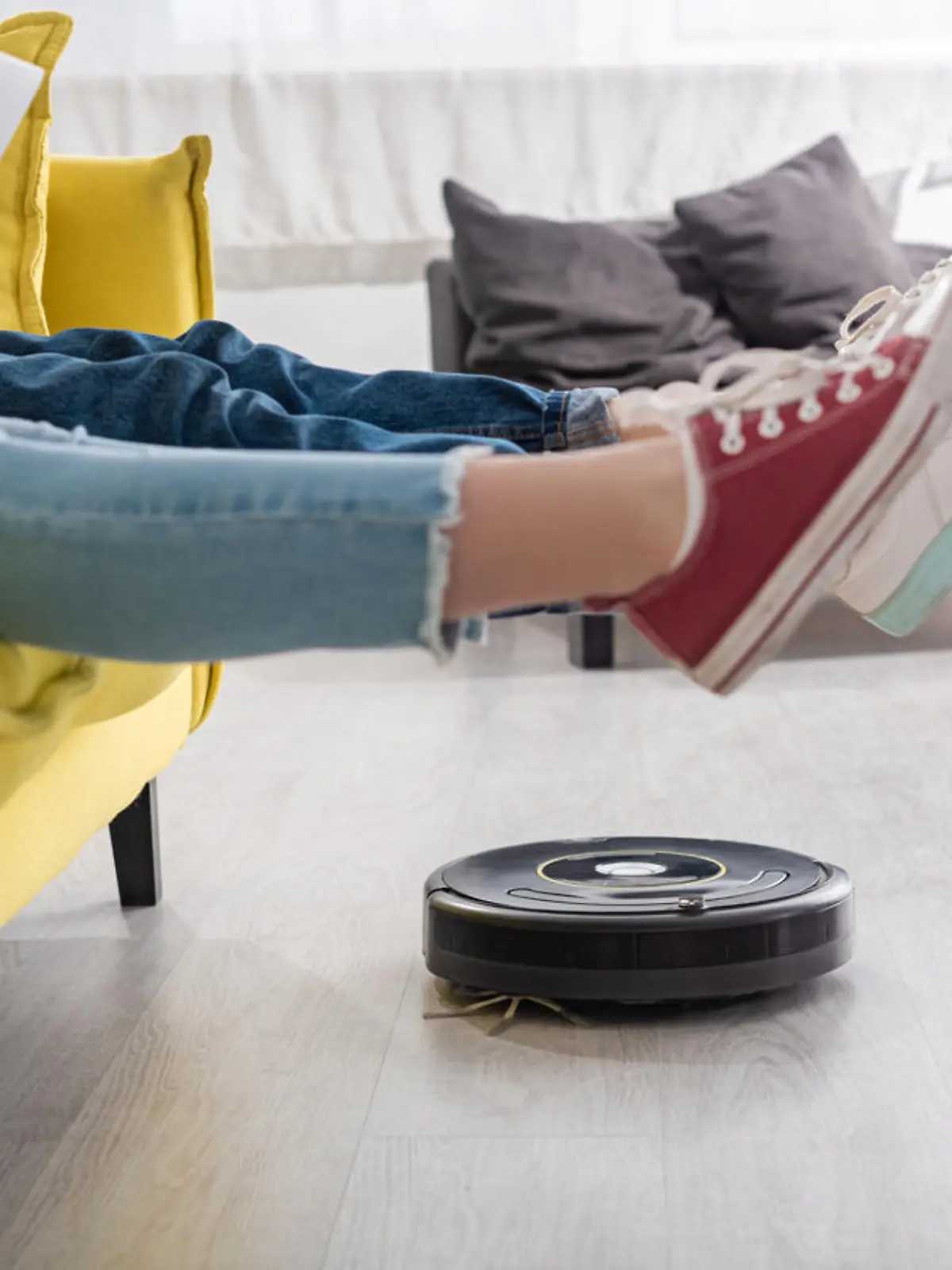 Cropped view of kid with laptop near mother with raised legs on sofa and robotic vacuum cleaner on floor in living room