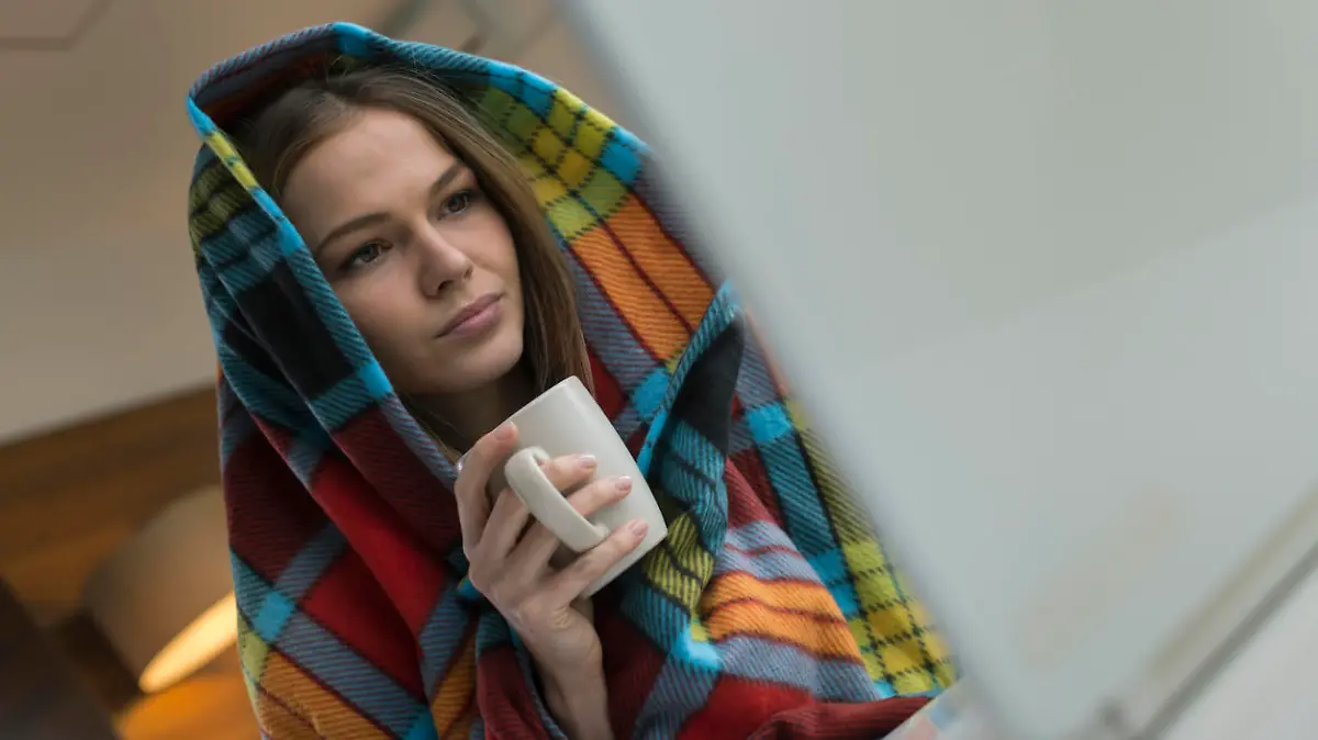Young woman which has a flu holding cup of tea and working from home on a laptop