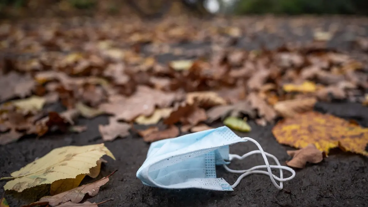 ARCHIV - 01.11.2020, Nordrhein-Westfalen, Herdecke: Eine weggeworfene Maske liegt zwischen Herbstlaub auf einer Straße, während ein Radfahrer vorbeifährt. Nordrhein-Westfalen lockert weiter. Im Freien müssen keine Masken mehr getragen werden. Und auch bei Veranstaltungen und in der Gastronomie gibt es weitere Lockerungen. (zu dpa: «Keine Maskenpflicht mehr im Freien») Foto: Bernd Thissen/dpa +++ dpa-Bildfunk +++