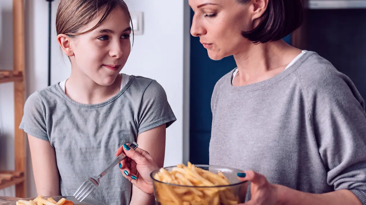 Mother serving French fries to her daughter for lunch at home