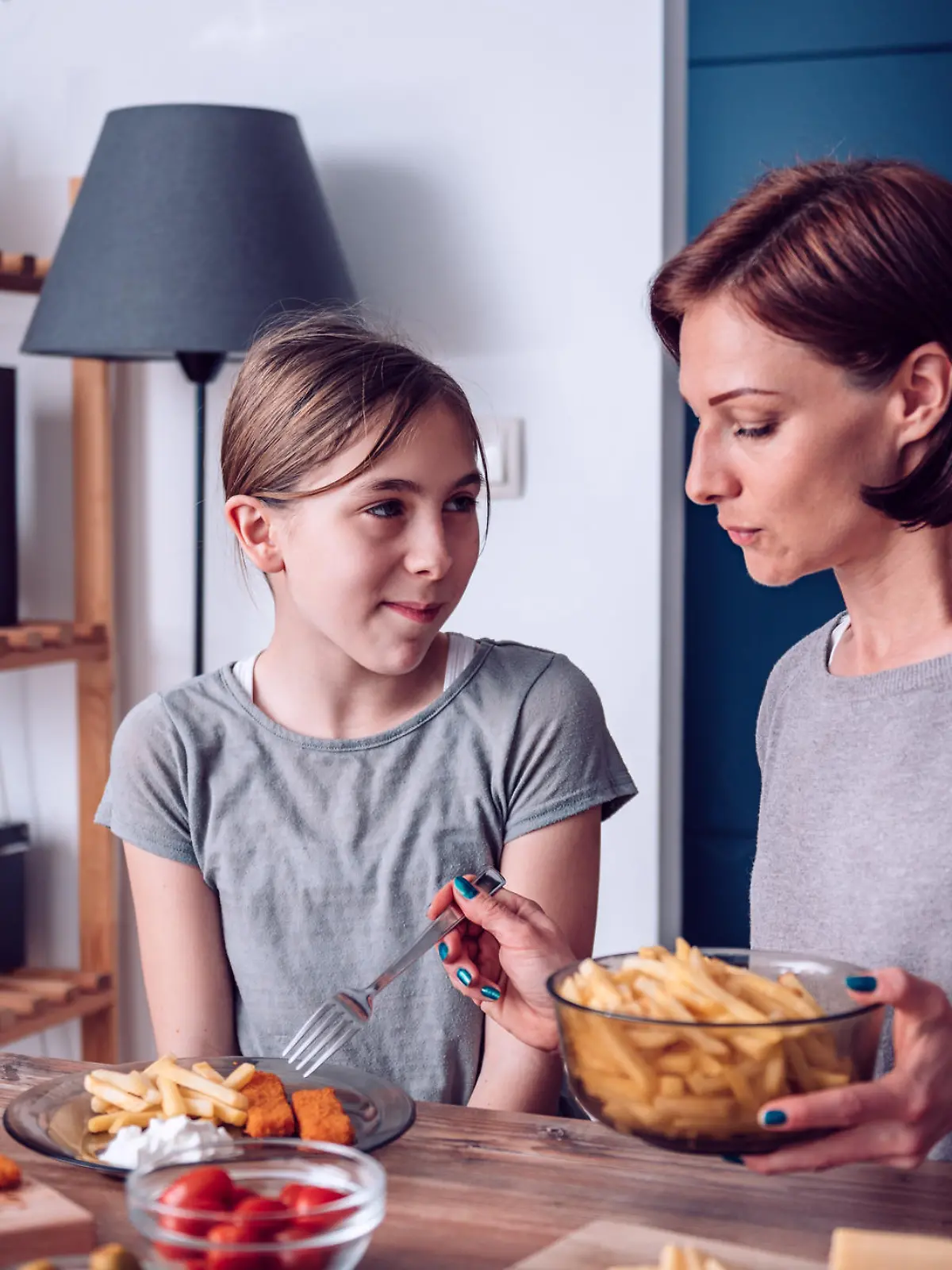 Mother serving French fries to her daughter for lunch at home