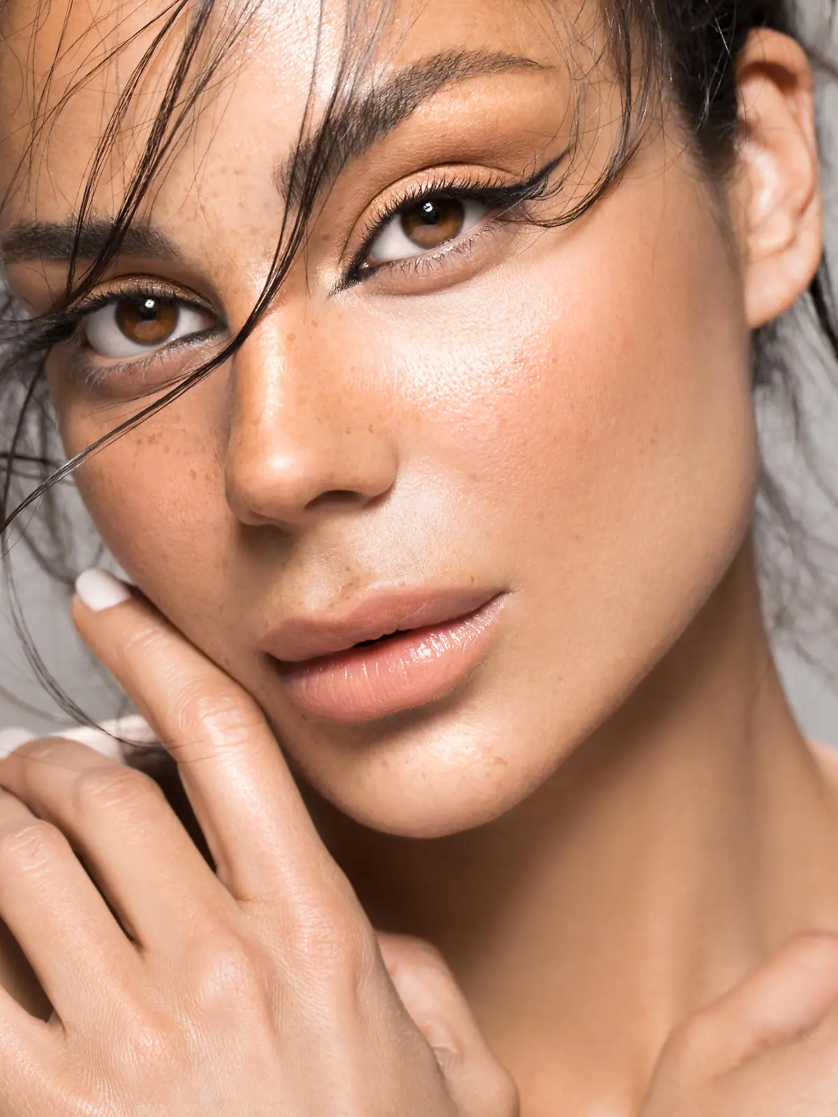 Close up studio shot of a beautiful brunette woman with glowing skin. Holding hands near her face.