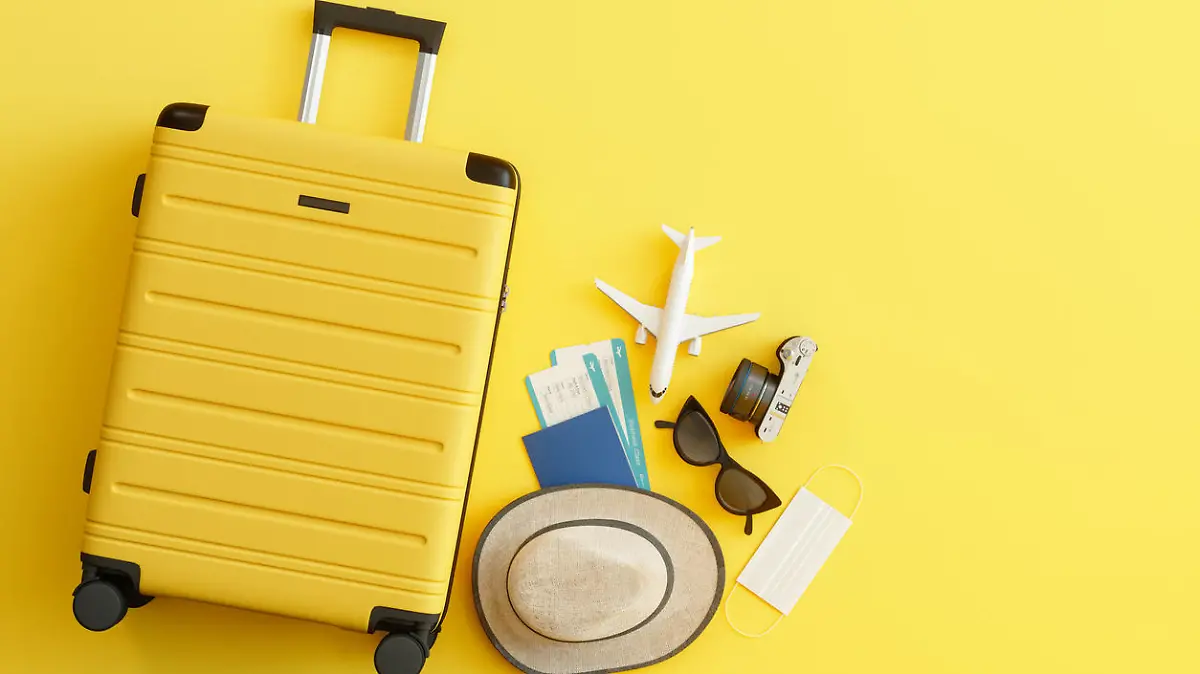 Medical Mask, Suitcase with Sun Hat, Camera, Passport, Airplane Ticket, Sunglasses and Airplane on Yellow Background