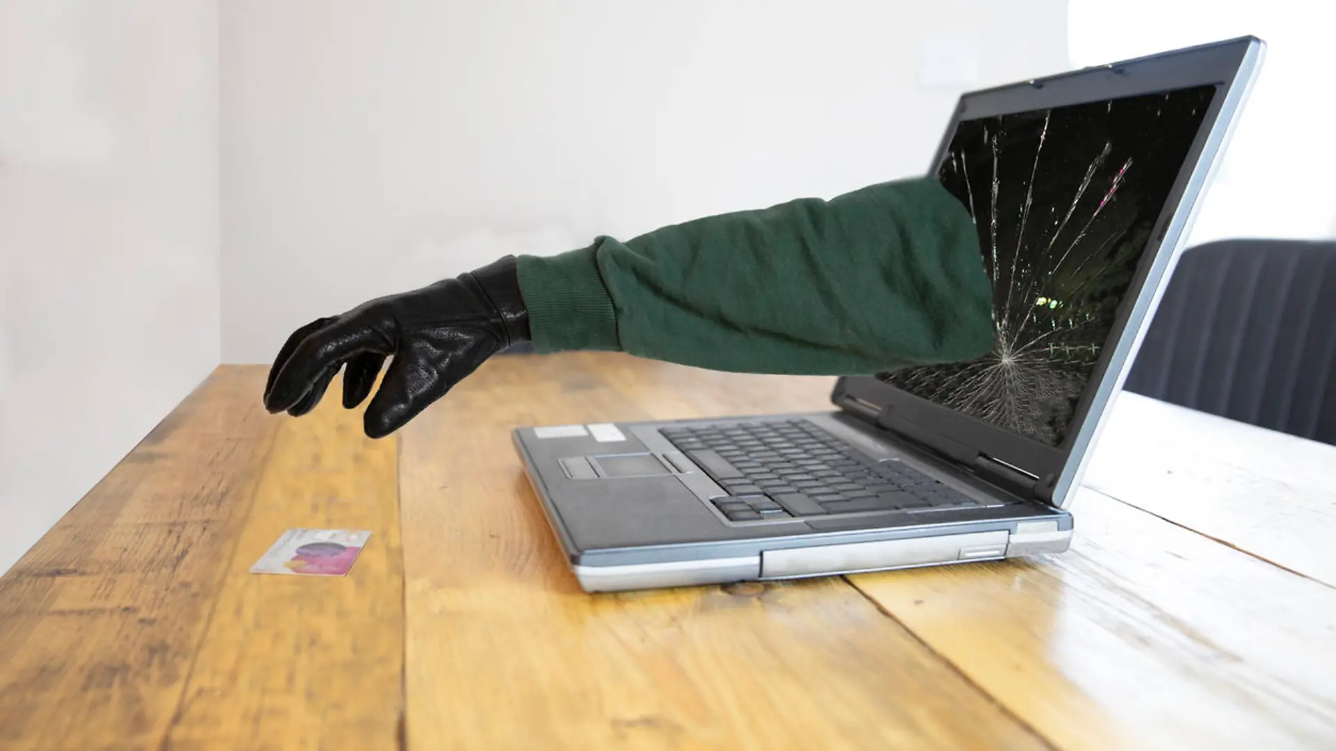 Laptop with black gloved hand coming through the screen stealing a credit card - internet fraud and theft