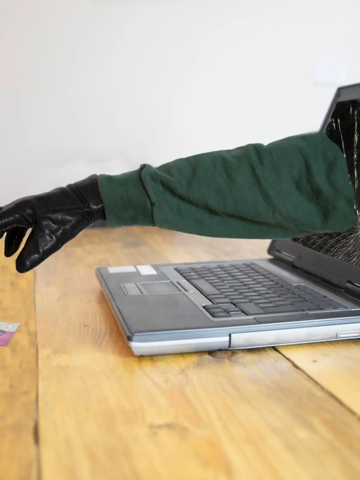 Laptop with black gloved hand coming through the screen stealing a credit card - internet fraud and theft