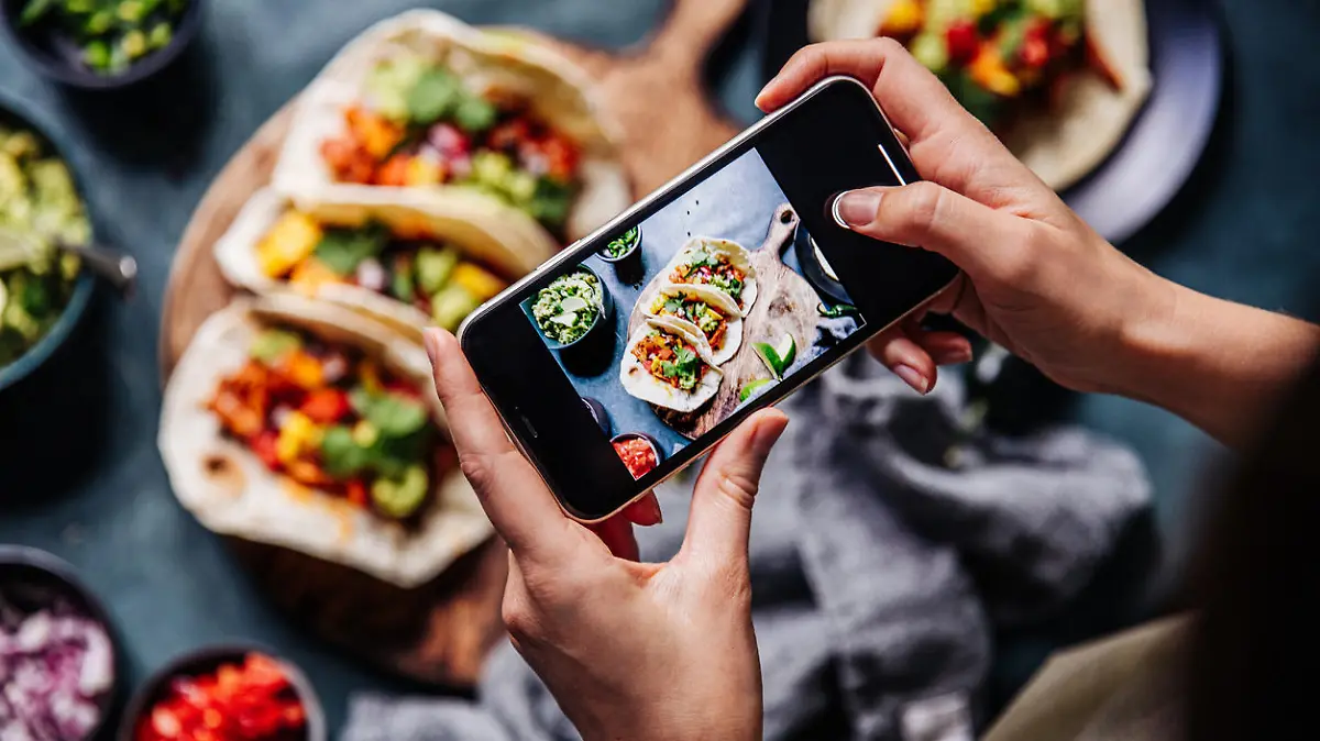 Hand of a chef taking photograph of tacos on table with a mobile phone. Hands of cook photographing Mexican food .