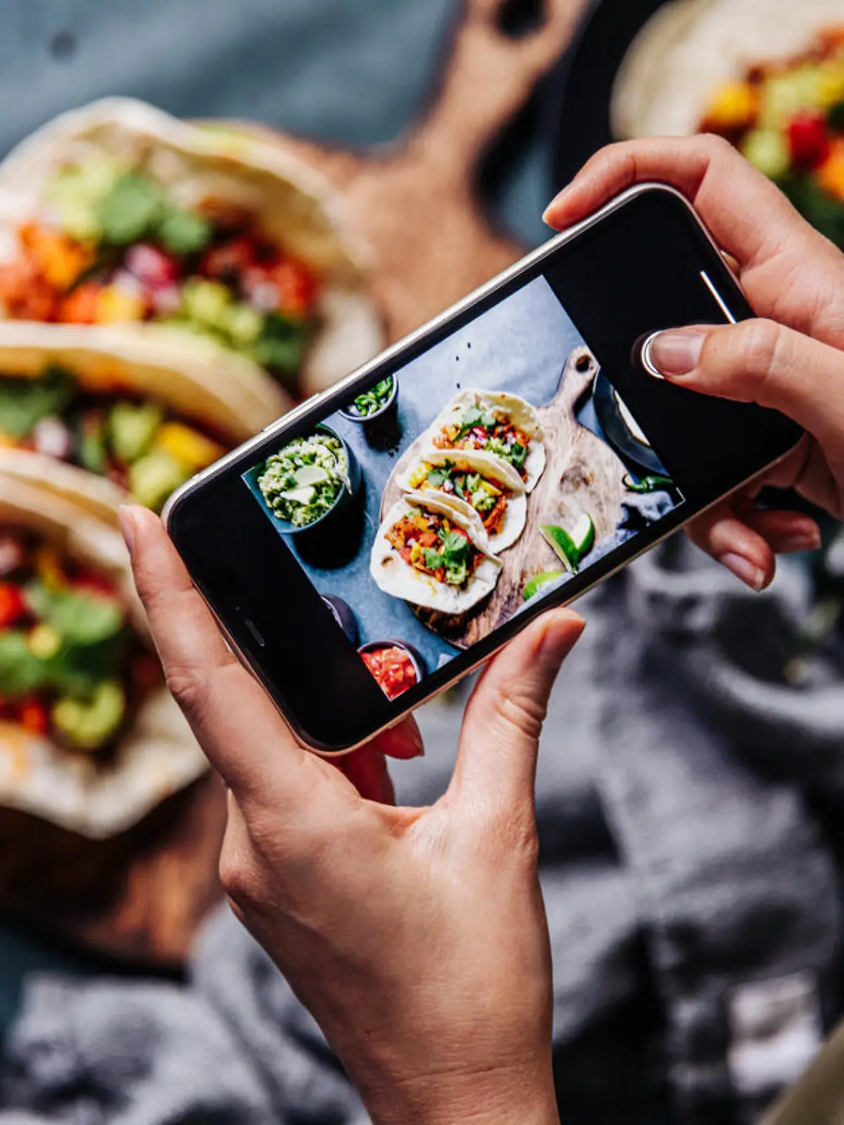 Hand of a chef taking photograph of tacos on table with a mobile phone. Hands of cook photographing Mexican food .
