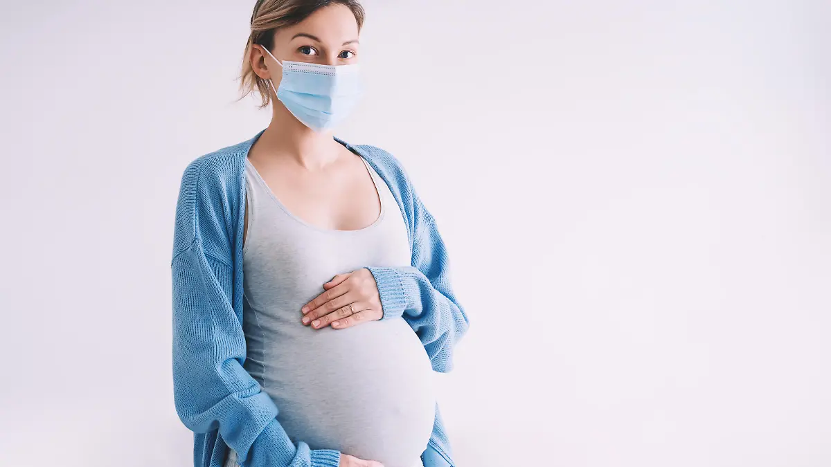 Young pregnant woman in medical mask hugging belly. Concept protection and prevention during viruses, mother care of her and unborn baby health. Pregnancy and childbirth during infectious diseases.