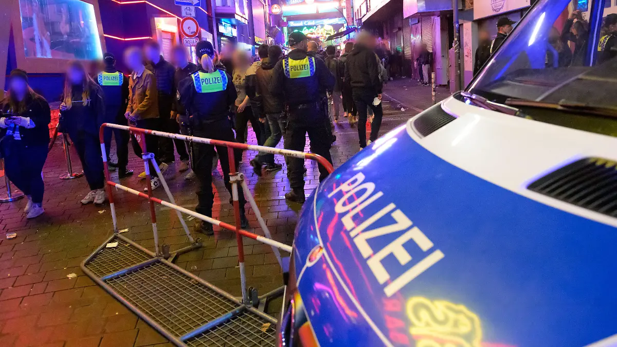 19.09.2021, Hamburg: Polizisten stehen neben ihrem Fahrzeug und einem Absperrgitter vor der Großen Freiheit. Trotz voller Straßen, Bars und Restaurants haben sich die Besucher auf der Reeperbahn am Wochenende weitgehend an die Corona-Regeln gehalten. In der Nacht zu Samstag seien in der Spitze rund 11 000 Feiernde unterwegs gewesen und in der Nacht darauf in der Spitze bis zu 25 000 Menschen, wie eine Polizeisprecherin am Sonntag in Hamburg sagte. Foto: Jonas Walzberg/dpa - ACHTUNG: Person(en) wurde(n) aus rechtlichen Gründen gepixelt +++ dpa-Bildfunk +++
