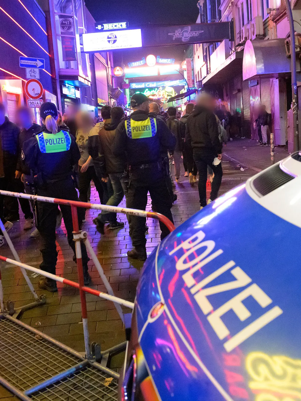 19.09.2021, Hamburg: Polizisten stehen neben ihrem Fahrzeug und einem Absperrgitter vor der Großen Freiheit. Trotz voller Straßen, Bars und Restaurants haben sich die Besucher auf der Reeperbahn am Wochenende weitgehend an die Corona-Regeln gehalten. In der Nacht zu Samstag seien in der Spitze rund 11 000 Feiernde unterwegs gewesen und in der Nacht darauf in der Spitze bis zu 25 000 Menschen, wie eine Polizeisprecherin am Sonntag in Hamburg sagte. Foto: Jonas Walzberg/dpa - ACHTUNG: Person(en) wurde(n) aus rechtlichen Gründen gepixelt +++ dpa-Bildfunk +++