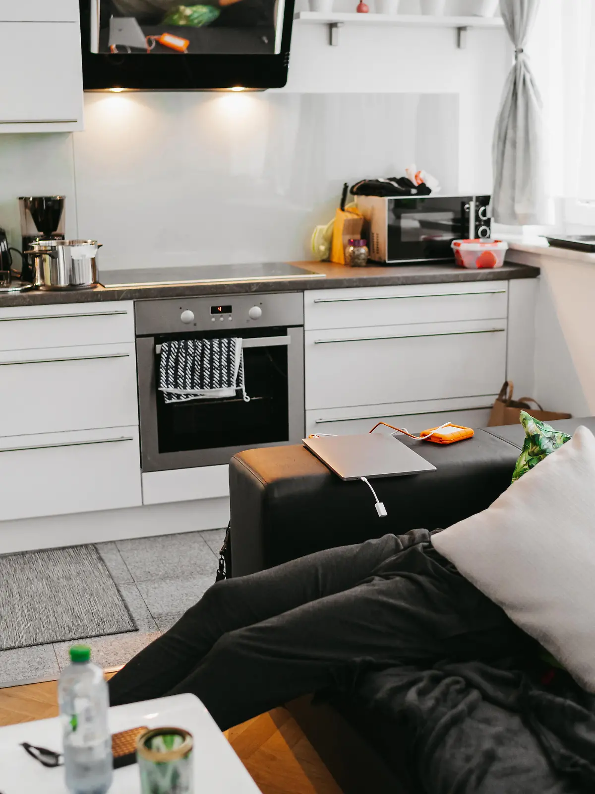 Young woman preparing food in kitchen while man sleeping on sofa