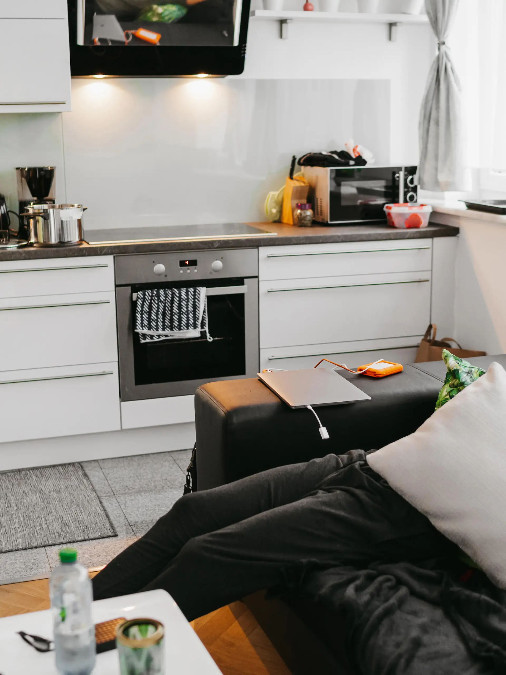 Young woman preparing food in kitchen while man sleeping on sofa