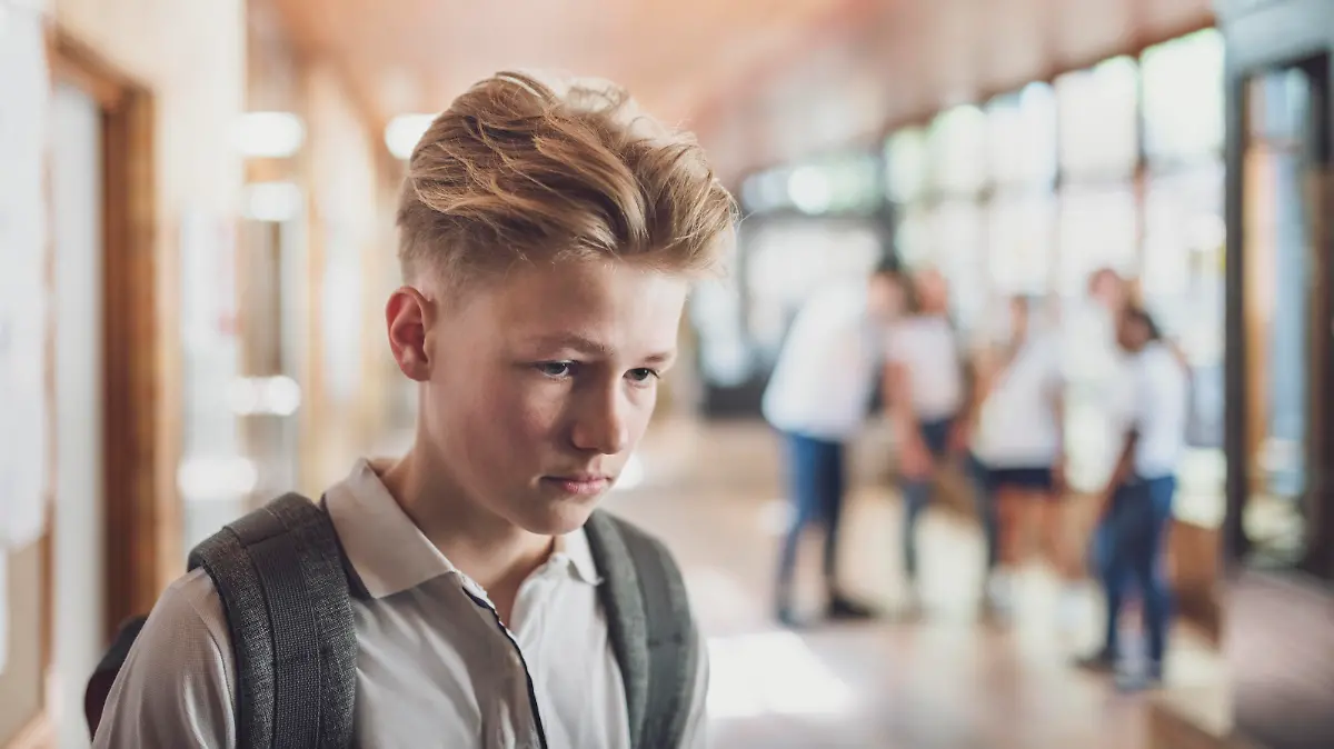 Teenage student being bullied by classmates in school. Sad boy is looking away. University students are making fun of him in corridor.