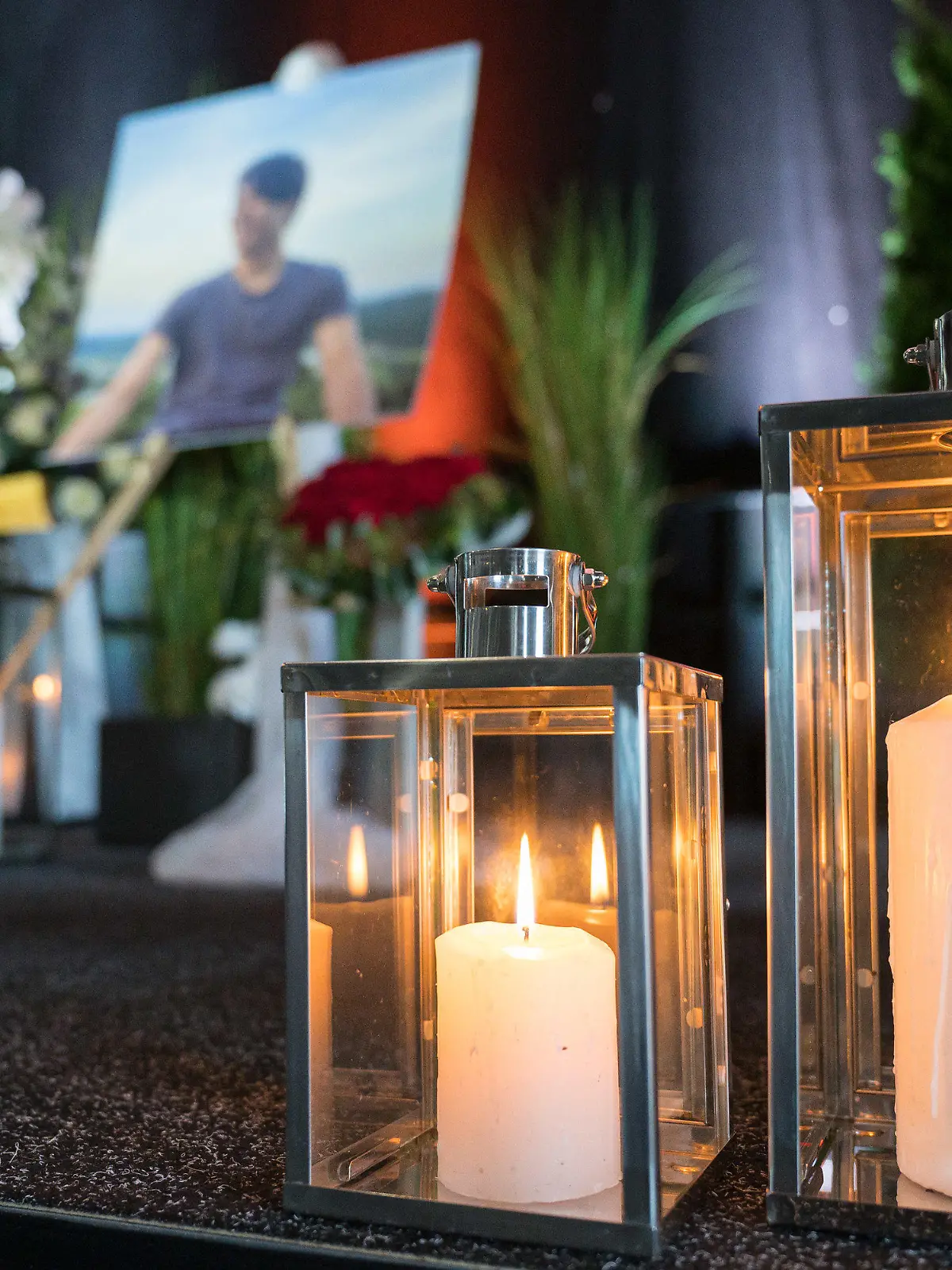 07.10.2021, Rheinland-Pfalz, Idar-Oberstein: Kerzen, ein Portrait und ein Kreuz mit dem Namen des getöteten Tankstellen-Mitarbeiters stehen bei der Trauerfeier auf der Bühne. Ein Mitarbeiter der Tankstelle war am 18. September von einem Mann erschossen worden. Das Opfer hatte den Kunden auf die Maskenpflicht hingewiesen, da dieser ohne Maske Bier kaufen wollte. Foto: Oliver Dietze/dpa - ACHTUNG: Nur zur redaktionellen Verwendung und nur mit vollständiger Nennung des vorstehenden Credits. Verwendung nur im vollen Ausschnitt. +++ dpa-Bildfunk +++