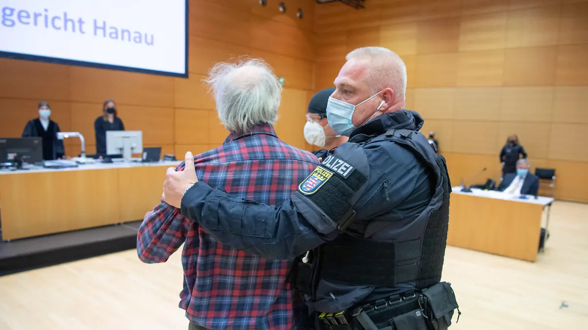 06.10.2021, Hessen, Hanau: Der Angeklagte wird von einem Polizisten in den Verhandlungssaal geführt. Der Mann ist der Vater des Attentäters von Hanau, der 2019 neun Menschen mit Migrationshintergrund aus rechstextremistischen Motiven ermordet hatte, bevor er vermutlich seine Mutter und schließlich sich selbst tötete. Der Mann muss sich jetzt wegen Beleidigung in mehreren Fällen verantworten. Foto: Boris Roessler/dpa +++ dpa-Bildfunk +++