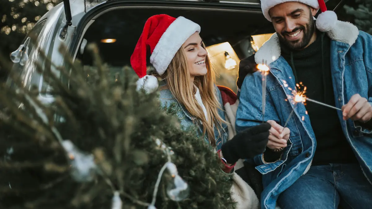 Happy couple is wearing Santa Claus hat and sitting in car trunk while enjoying their beautiful moments of Christmas tree adventure. It is a cold and sunny day outside.