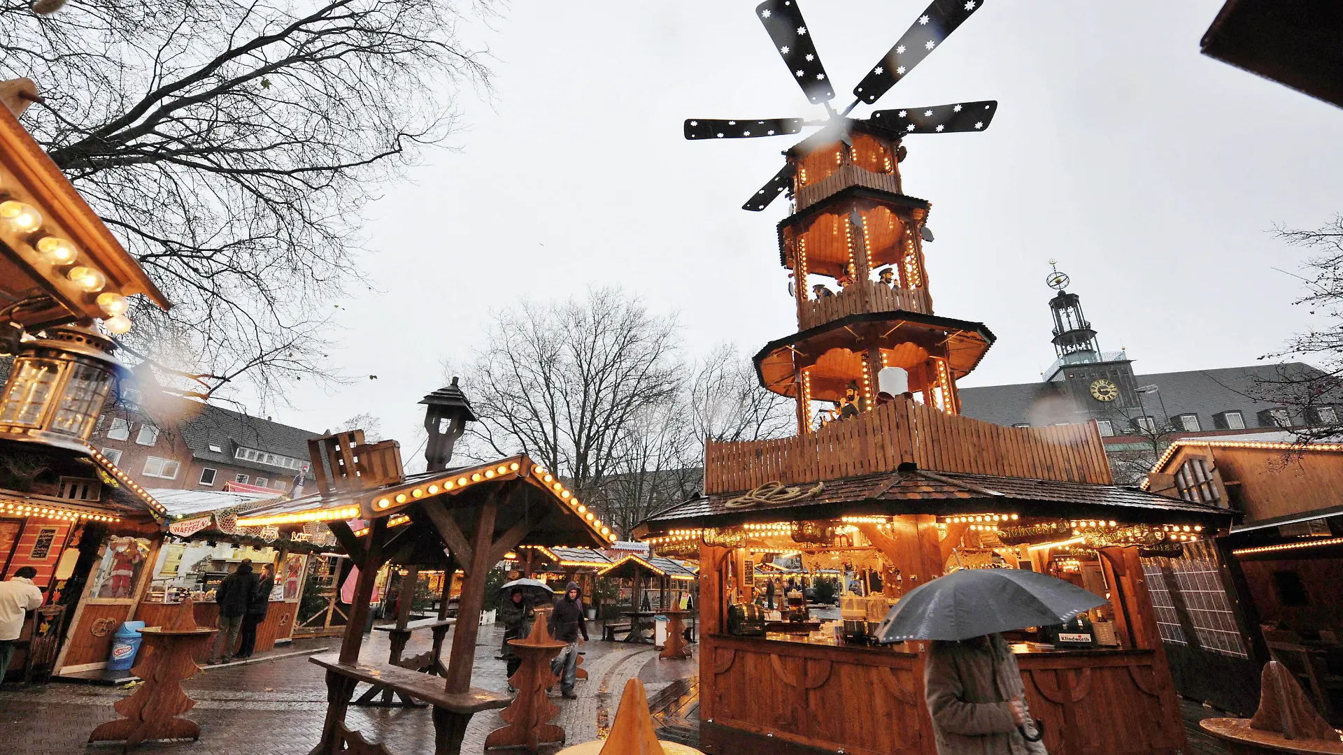 Mit einem Regenschirm geschützt geht am Dienstag (23.11.2010) eine Frau bei strömenden Regen über den neu gestalteten Weihnachtsmarkt in Emden an der zum ersten mal aufgestellten 12 Meter hohen Holzpyramide vorbei. Foto: Carmen Jaspersen dpa/lni +++(c) dpa - Bildfunk+++