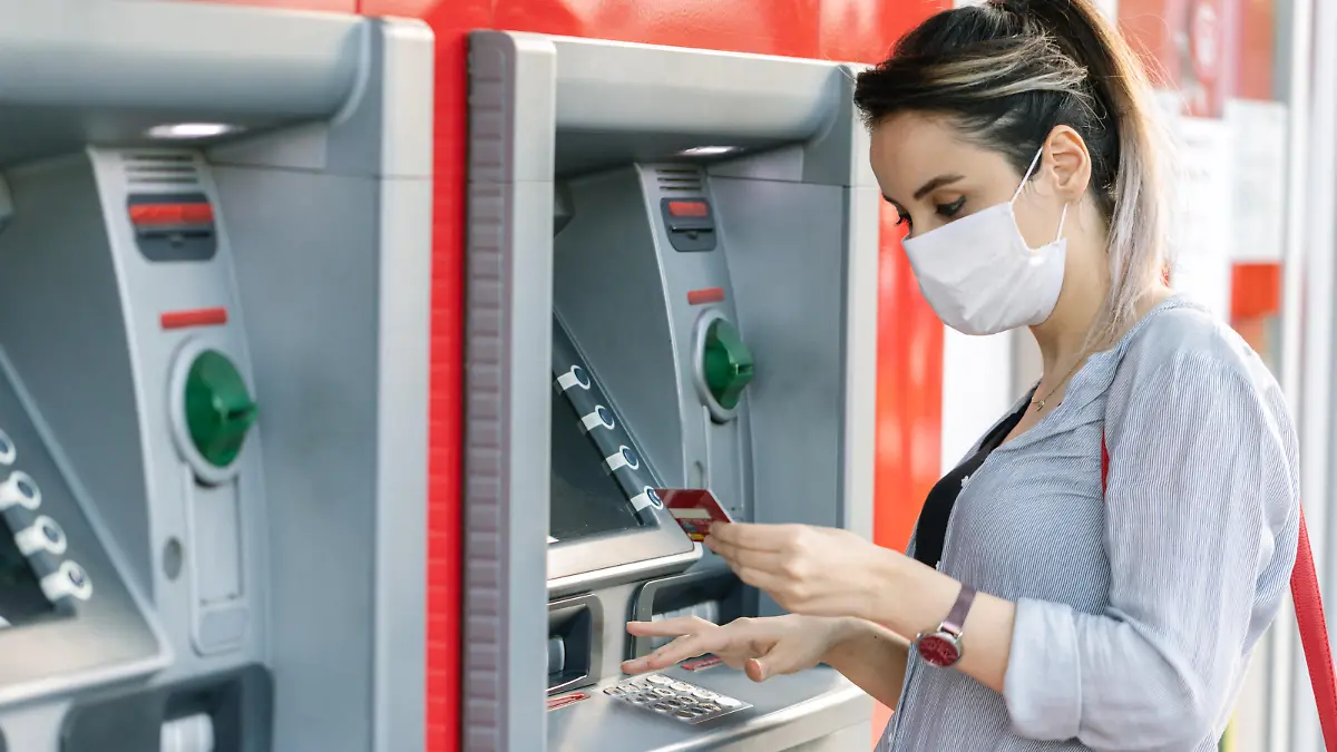 Young woman wearing protective face mask while withdrawing money at ATM