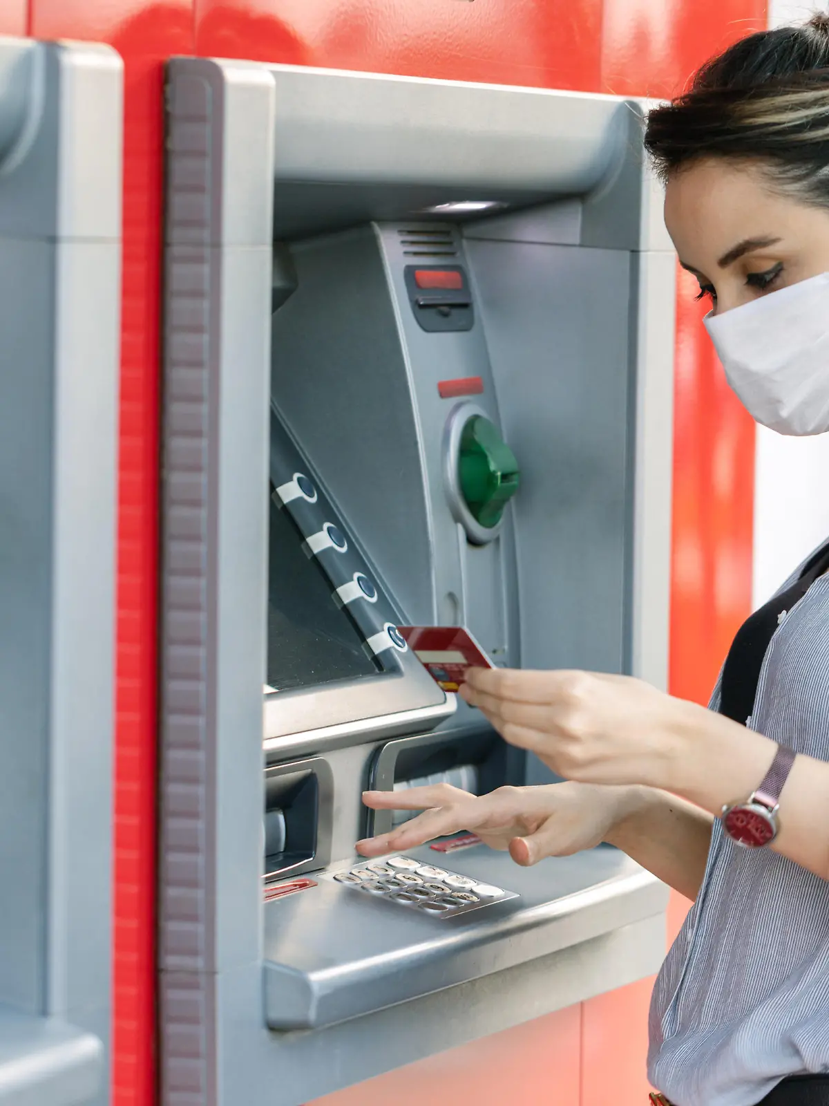 Young woman wearing protective face mask while withdrawing money at ATM
