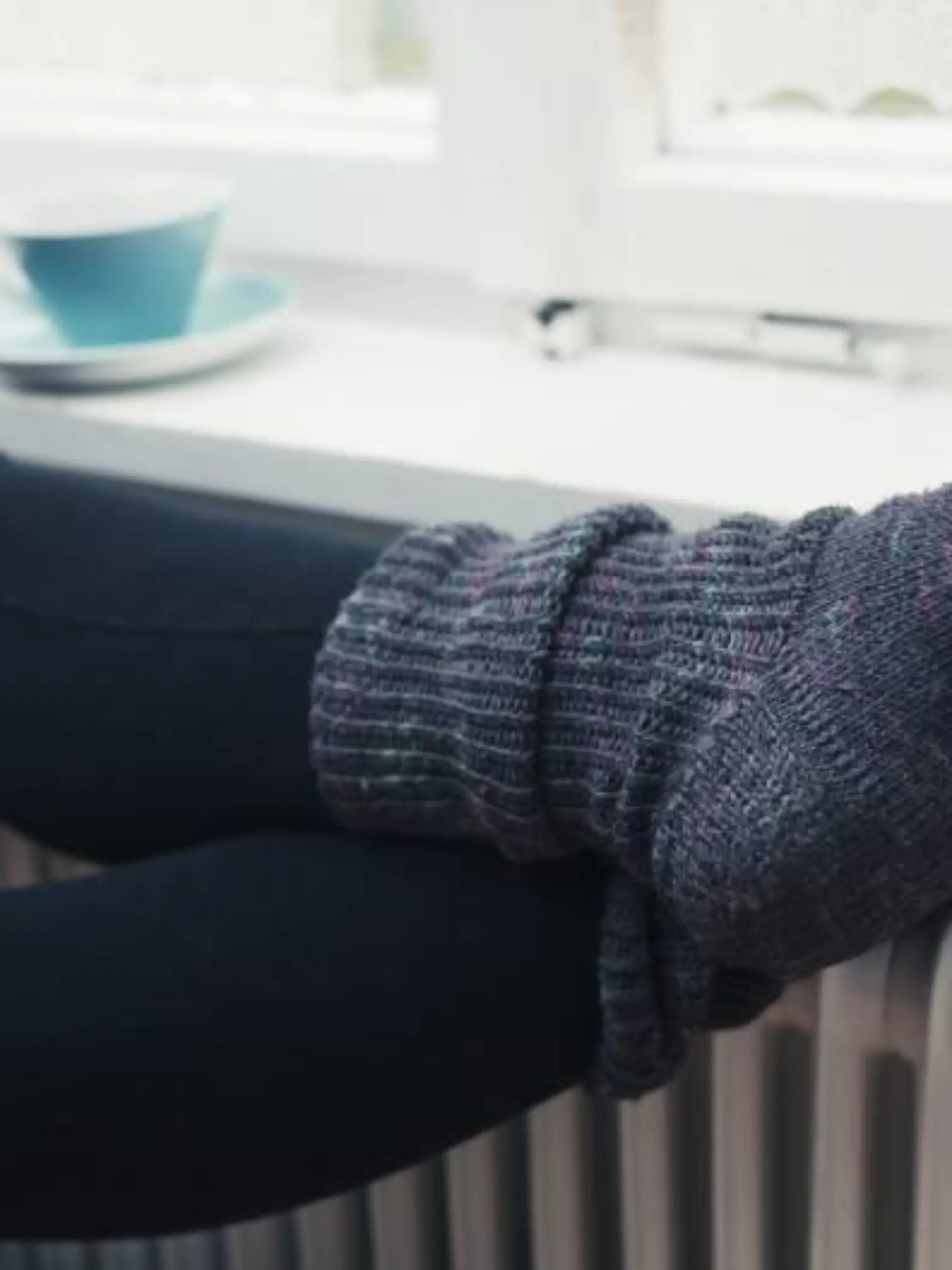 Frau mit dicken Socken und Tasse Tee legt Beine auf Heizung