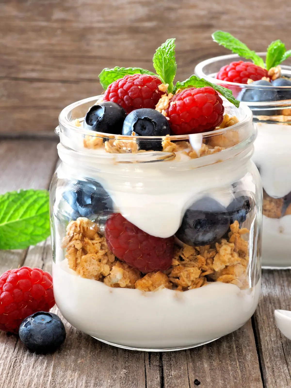Blueberry and raspberry parfaits in mason jars, still life against a rustic wood background