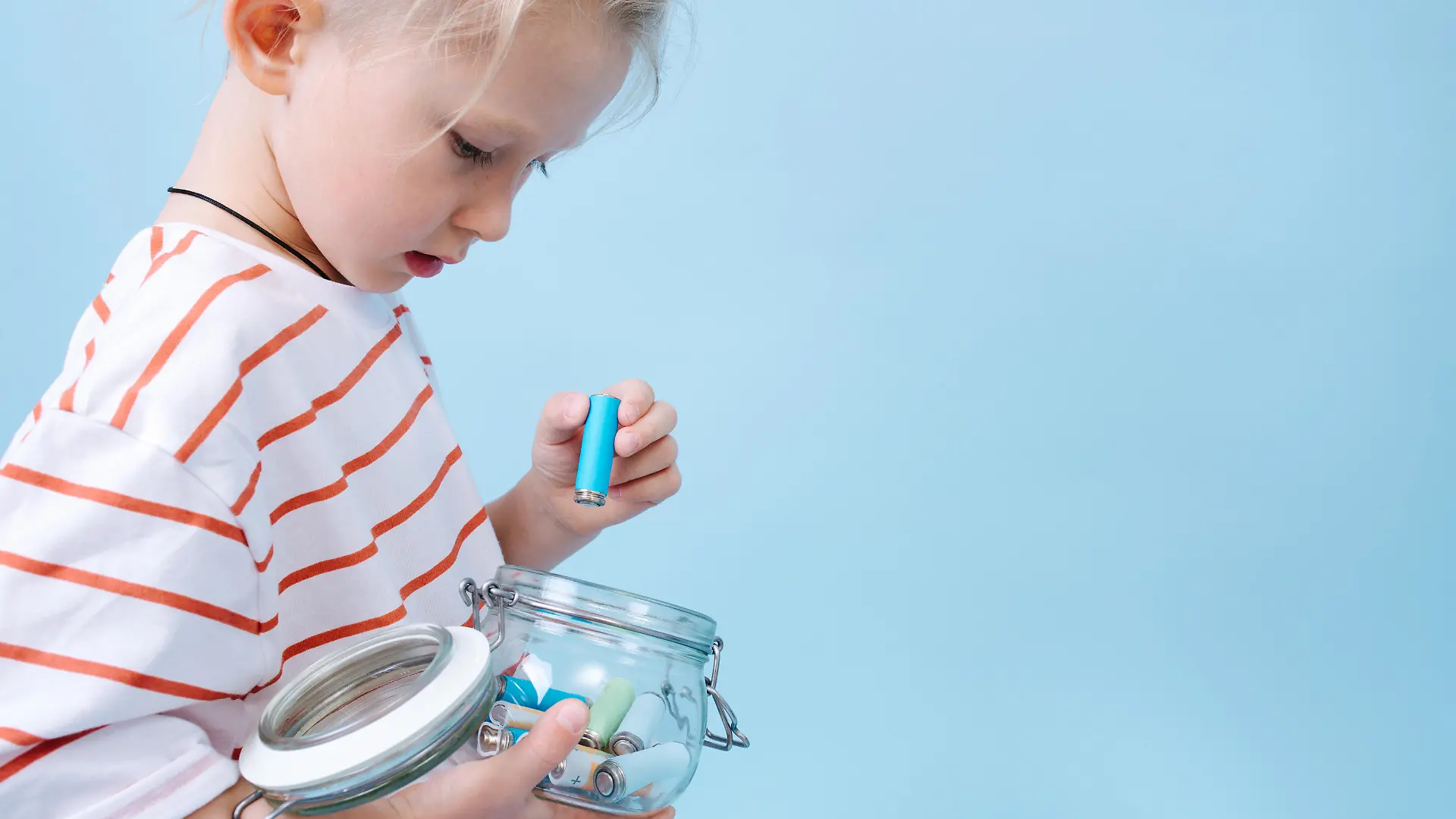Responsible thoughtful little boy is putting used batteries in a jar for recycling.
