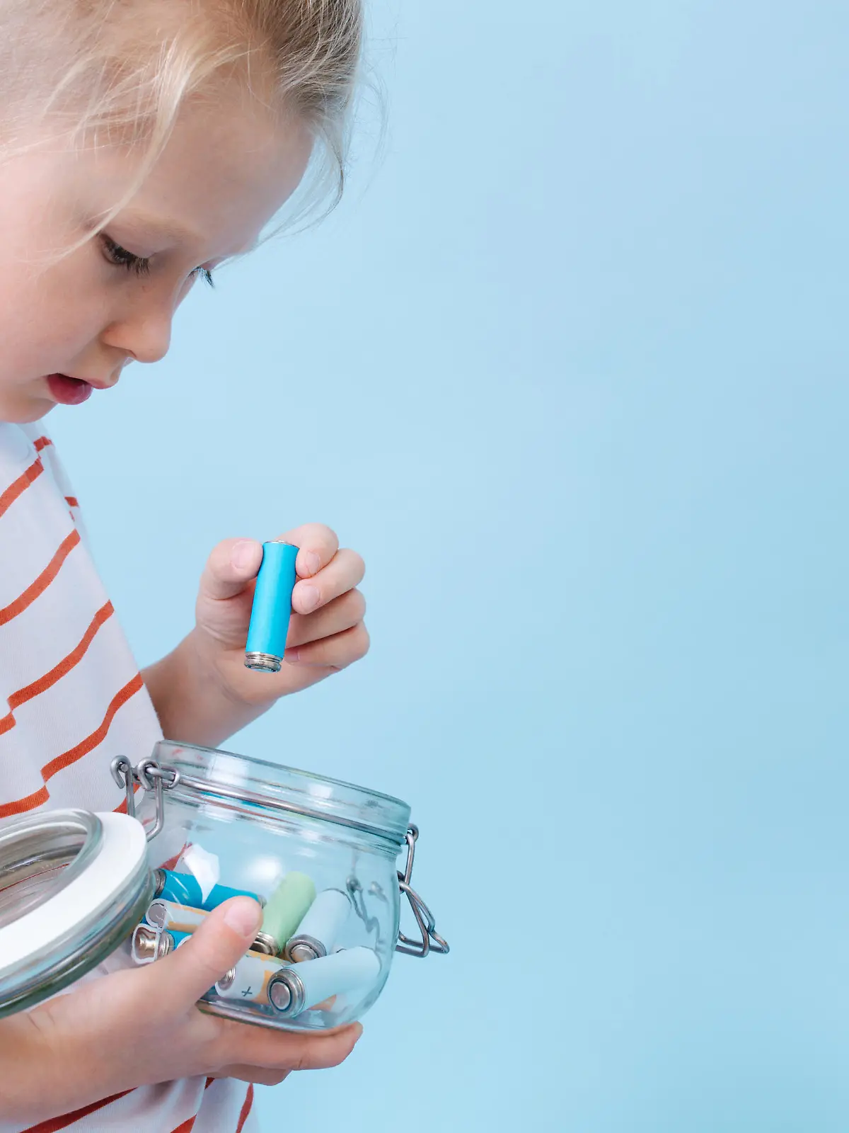 Responsible thoughtful little boy is putting used batteries in a jar for recycling.