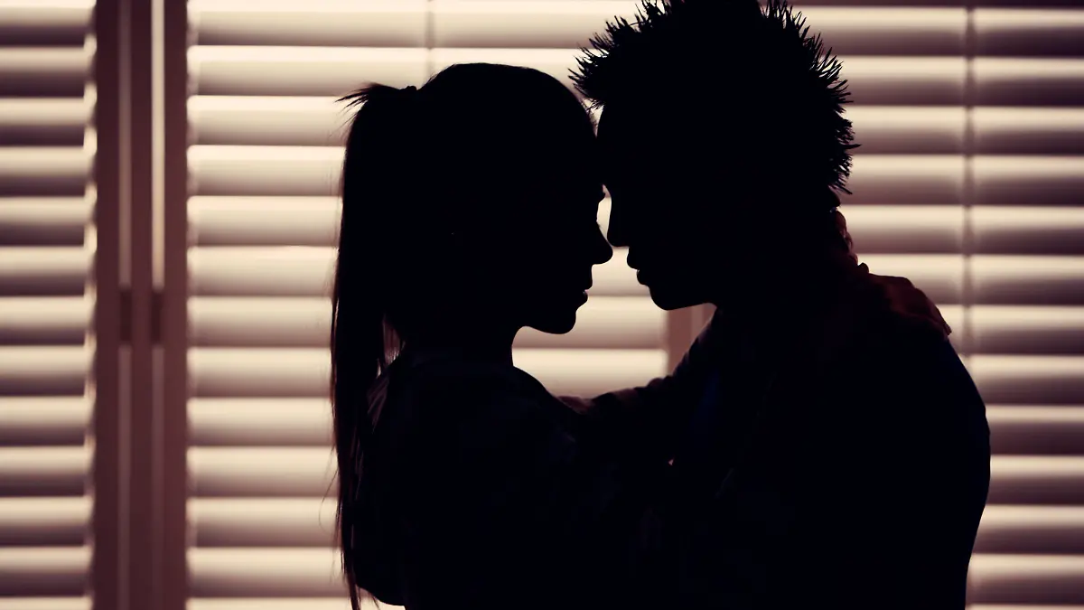 "Young couple in love share romantic embrace, presented in silhouette and the warm hues of dusk. Horizontal composition."