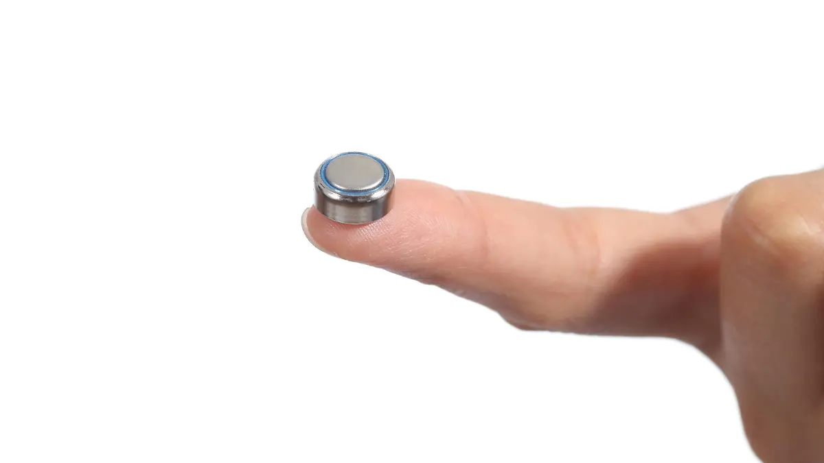Woman hand holding a button battery with the forefinger isolated on a white background