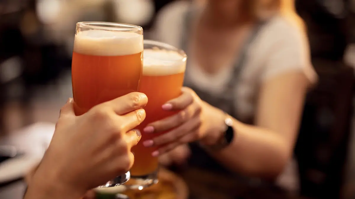 Close up of unrecognizable couple toasting with lager beer in a bar.
