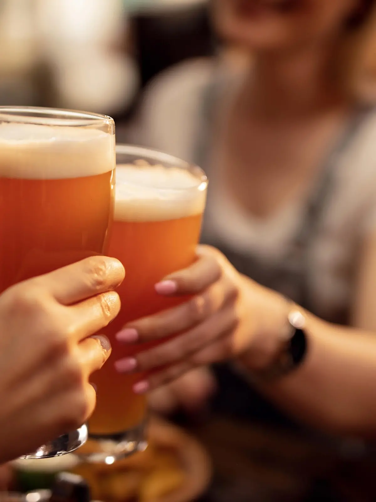 Close up of unrecognizable couple toasting with lager beer in a bar.