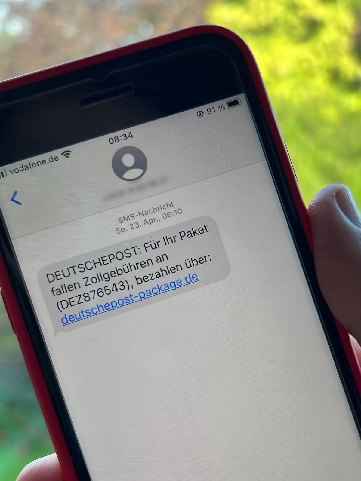 17.05.2023, Nordrhein-Westfalen, Düsseldorf: Ein Mann hält ein Smartphone mit einer betrügerischen SMS. Die Anzahl von betrügerischen SMS, in denen Verbraucher zur Zahlung von angeblichen Zollgebühren aufgefordert werden, hat stark zugenommen. In den SMS wird ein Paket angekündigt, das im Zoll festhänge. Erst wenn Zollgebühren entrichtet werden, werde die Sendung weitergeschickt, heißt es in den Betrugs-SMS, in denen auch ein Link steht. (Zu dpa: "Betrügerische Zollgebühren-SMS nehmen stark zu") Foto: Wolf von Dewitz/dpa - ACHTUNG: Telefonnummer wurde aus rechtlichen Gründen gepixelt +++ dpa-Bildfunk +++