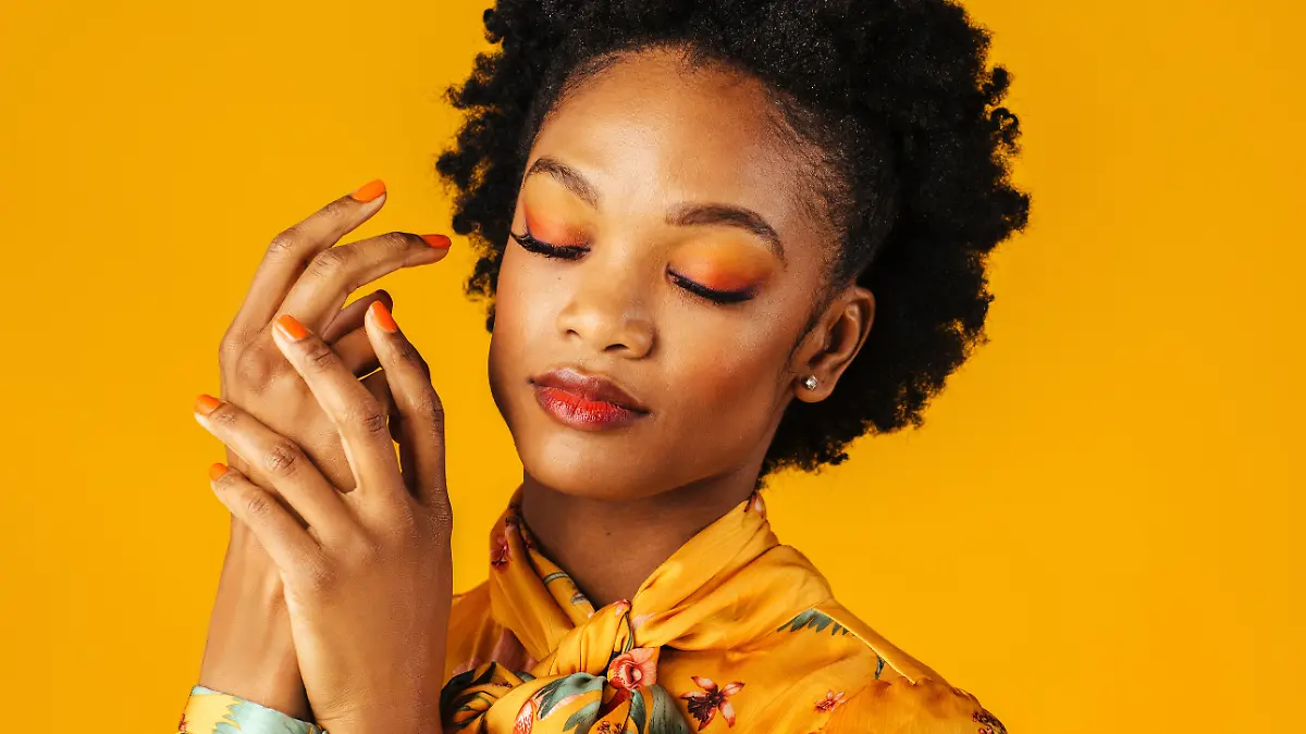 Portrait of a beautiful young woman with orange finger nails manicure,lips and eye shadow, isolated on yellow background