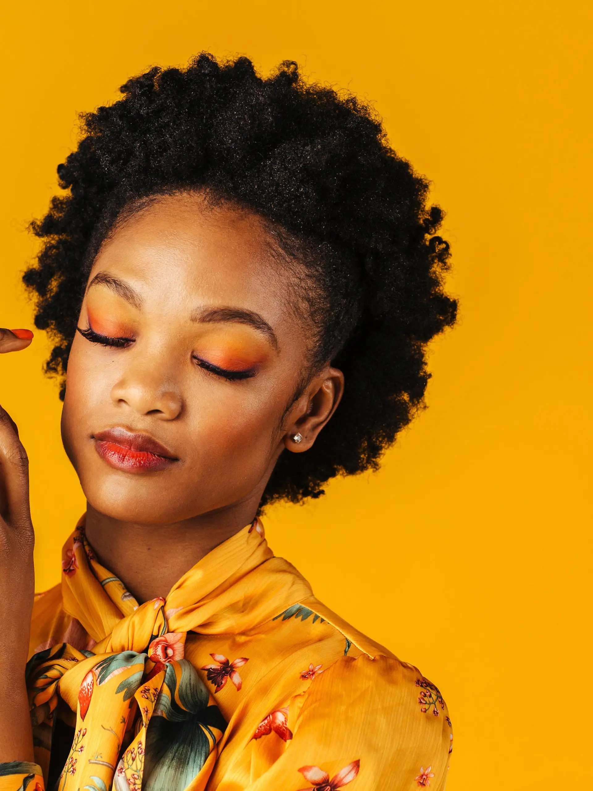 Portrait of a beautiful young woman with orange finger nails manicure,lips and eye shadow, isolated on yellow background