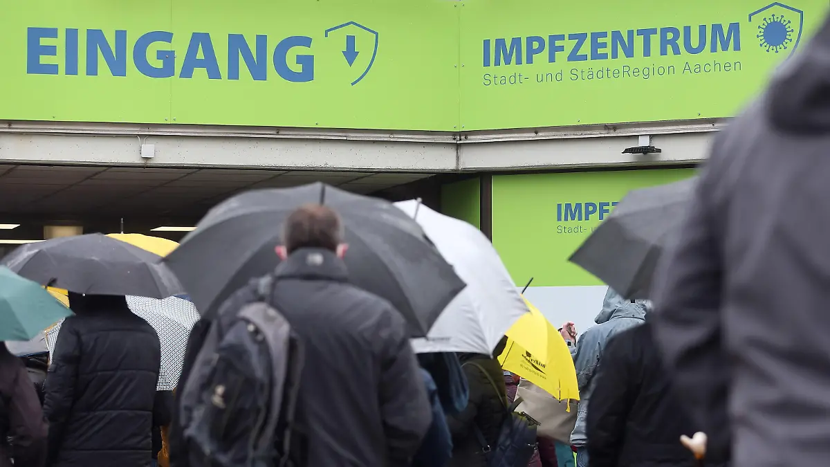 Menschen mit Regenschirme stehen vor dem Aachener Impfzentrum in einer Schlange.