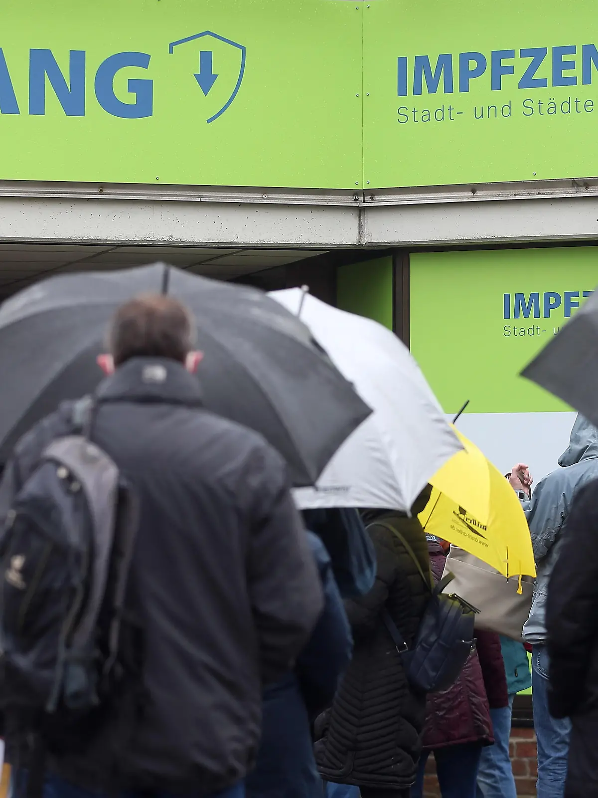 Menschen mit Regenschirme stehen vor dem Aachener Impfzentrum in einer Schlange.