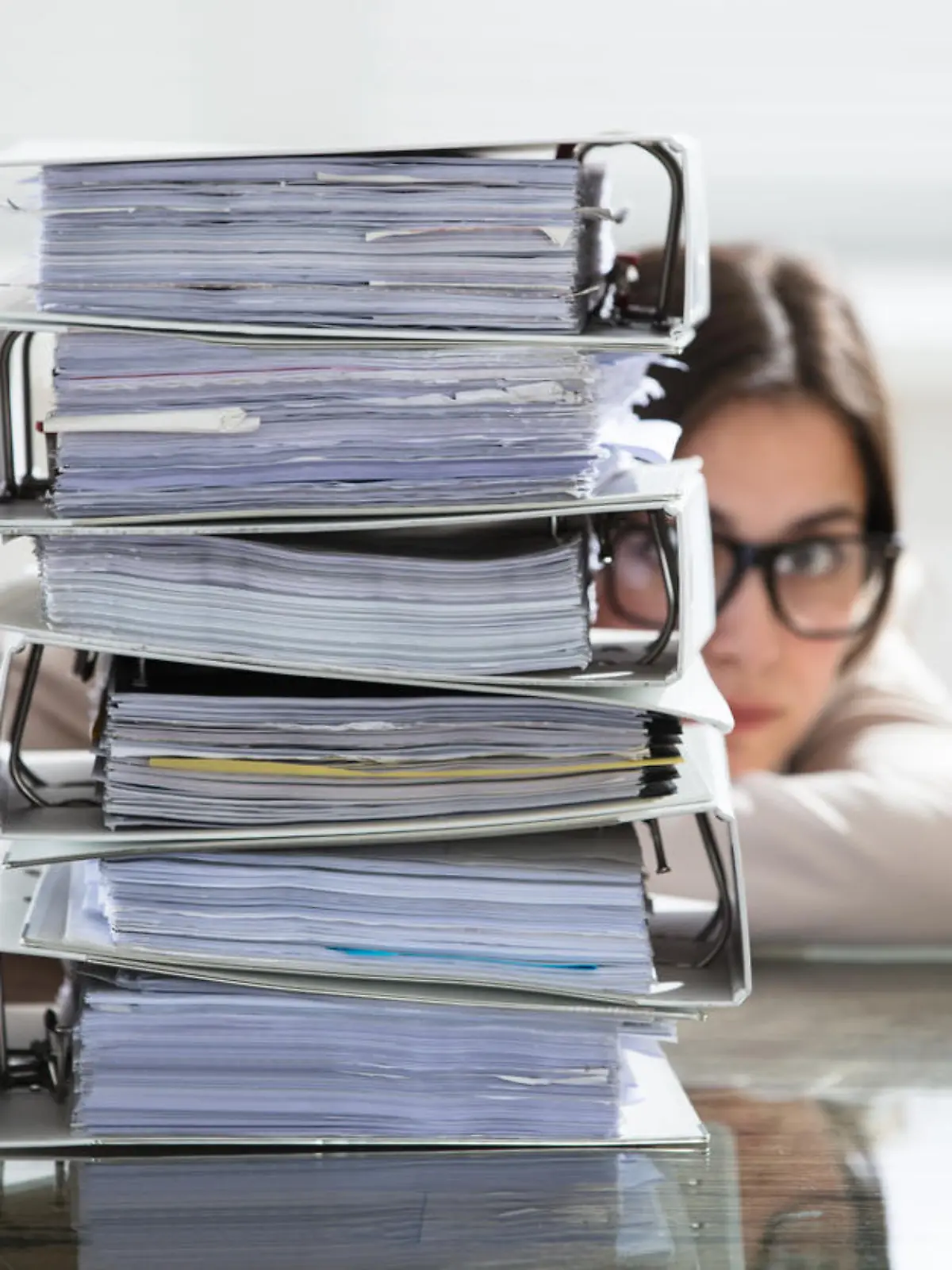Close-up Of A Businesswoman Hiding Behind The Stack Of Folders On Desk At Workplace
