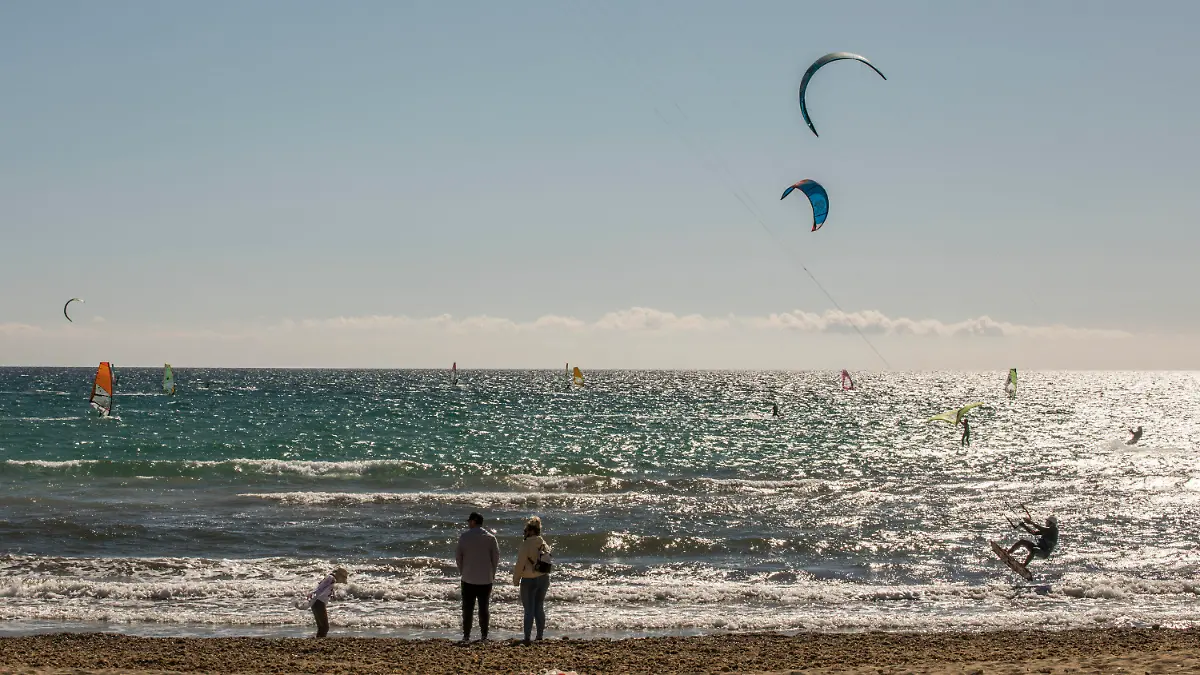 17.03.2021, Spanien, Mallorca: Eine Familie spaziert am Strand, während Kitesurfer den Tag das Meer vor Can Pastilla genießen. Schon vor dem Beginn der Osterferien ist auf der spanischen Mittelmeerinsel Mallorca die Zahl der Touristen gestiegen. Der größte Reiseanbieter Tui meldet kurz vor dem Start der vorgezogenen Ostersaison auf Mallorca anhaltend starke Buchungen. Foto: John-Patrick Morarescu/ZUMA Wire/dpa +++ dpa-Bildfunk +++