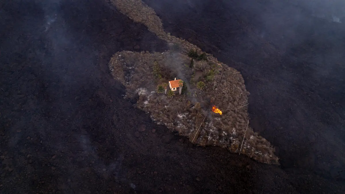 HANDOUT - 21.09.2021, Spanien, La Palma: Auf diesem von iLoveTheWorld zur Verfügung gestellten Foto bleibt ein Haus intakt, während Lava fließt, nachdem ein Vulkan in der Nähe von Las Manchas auf der Insel La Palma ausgebrochen ist. Der Vulkan war am 19. September erstmals seit 50 Jahren wieder aktiv geworden. Foto: Alfonso Escalero/iLoveTheWorld/dpa - ACHTUNG: Nur zur redaktionellen Verwendung im Zusammenhang mit der aktuellen Berichterstattung und nur mit vollständiger Nennung des vorstehenden Credits. Verwendung nur bis zum 04.10.2021 +++ dpa-Bildfunk +++