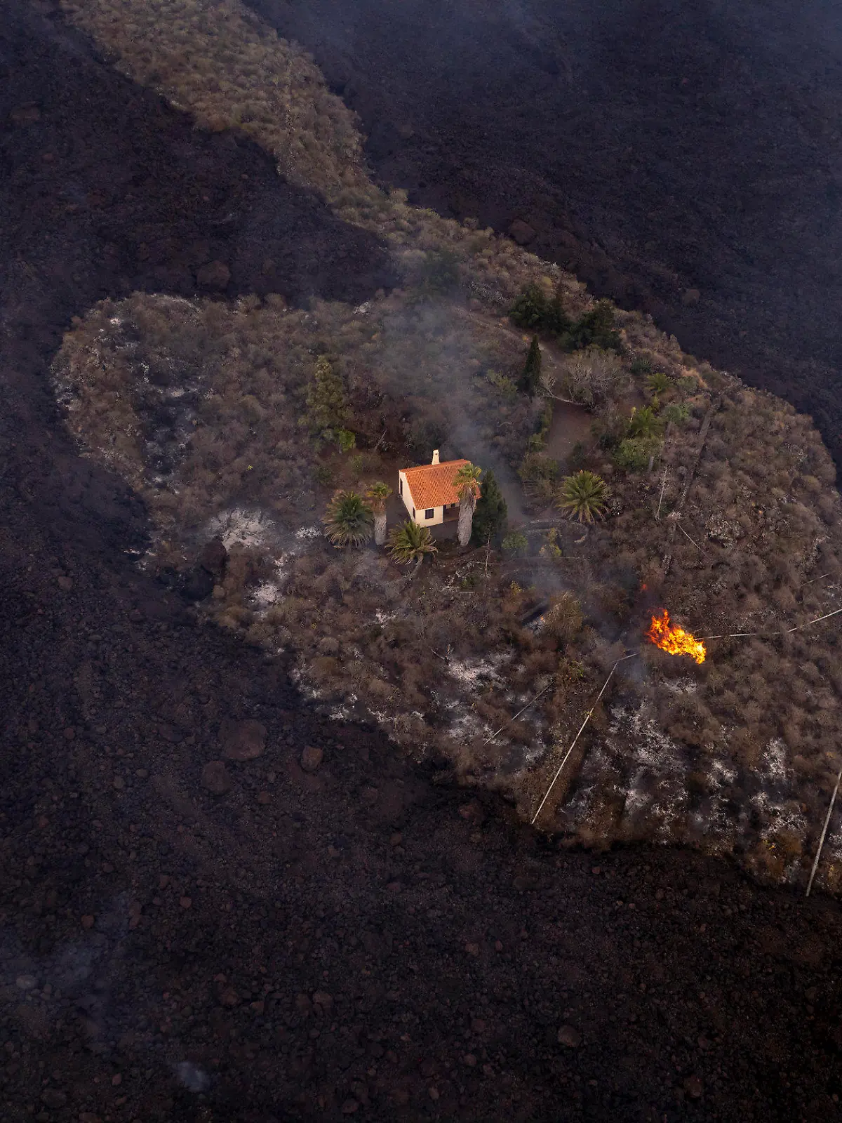 HANDOUT - 21.09.2021, Spanien, La Palma: Auf diesem von iLoveTheWorld zur Verfügung gestellten Foto bleibt ein Haus intakt, während Lava fließt, nachdem ein Vulkan in der Nähe von Las Manchas auf der Insel La Palma ausgebrochen ist. Der Vulkan war am 19. September erstmals seit 50 Jahren wieder aktiv geworden. Foto: Alfonso Escalero/iLoveTheWorld/dpa - ACHTUNG: Nur zur redaktionellen Verwendung im Zusammenhang mit der aktuellen Berichterstattung und nur mit vollständiger Nennung des vorstehenden Credits. Verwendung nur bis zum 04.10.2021 +++ dpa-Bildfunk +++
