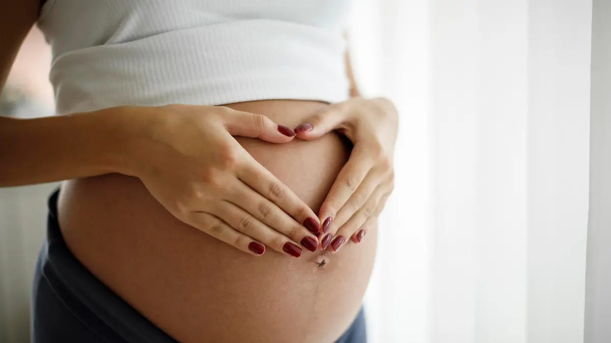 Pregnant woman holding her belly and making a heart shape