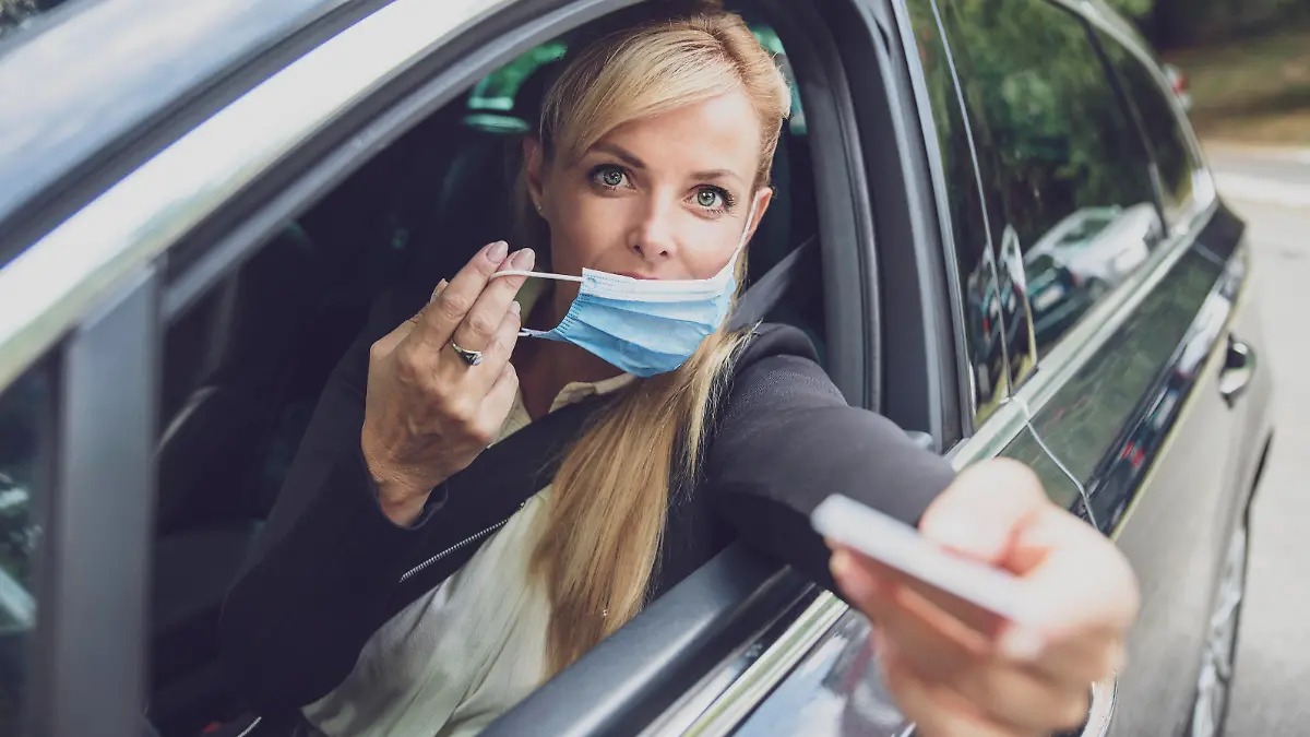 Female driver with protective face mask paying from the car or giving ID on the border.