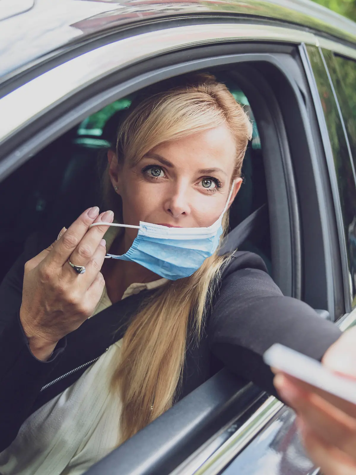 Female driver with protective face mask paying from the car or giving ID on the border.