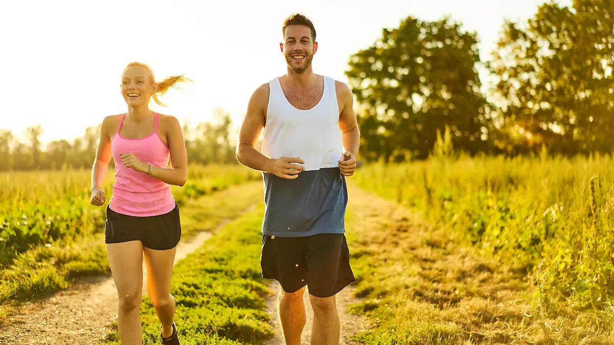 happy smiling young woman and man jogging on field path on sunny summer afternoon