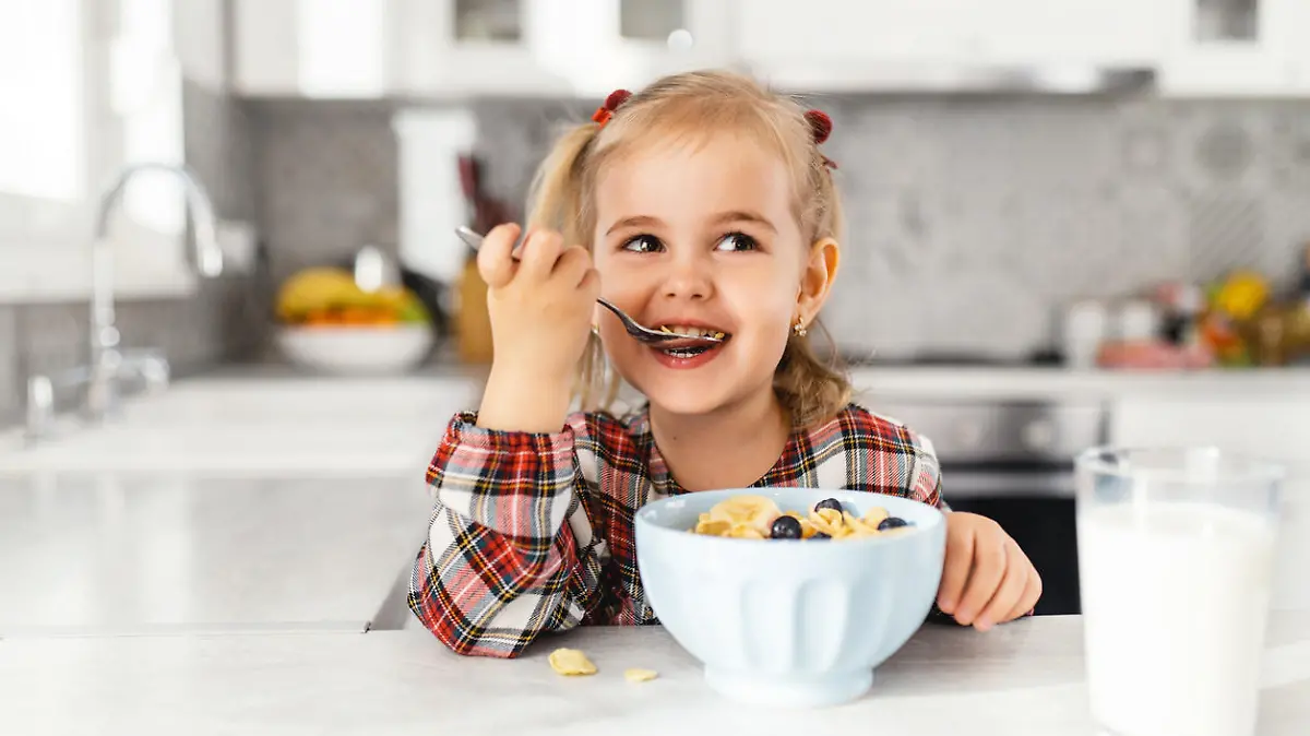 Beautiful little girl having breakfast with cereal, milk and blueberry in kitchen
