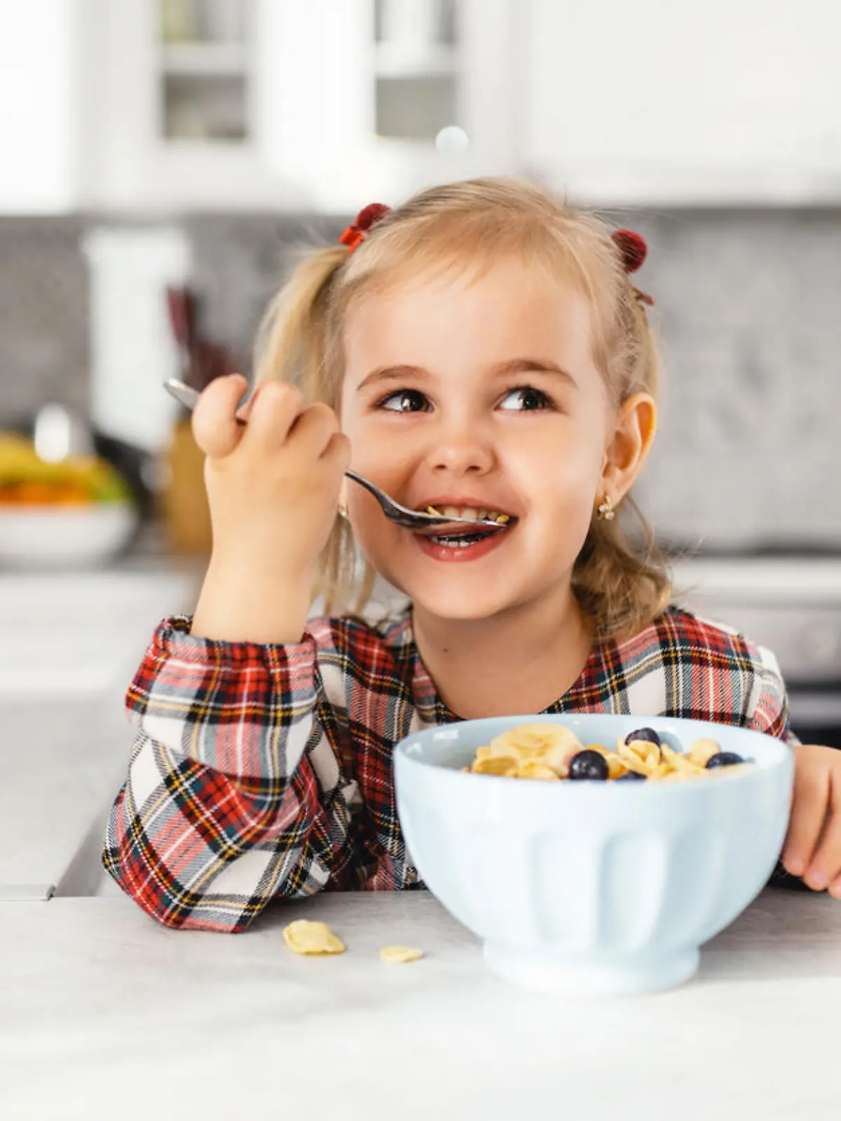 Beautiful little girl having breakfast with cereal, milk and blueberry in kitchen